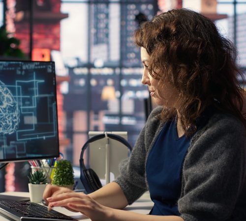 Female system admin doing maintenance on AI brain pc systems, sitting at office desk. Girl works as a software developer with cybernetics and algorithms for machine learning. Camera B.